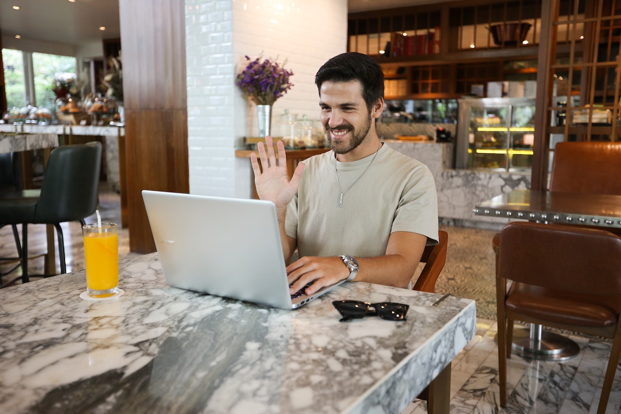 man waving to a laptop while working remotely