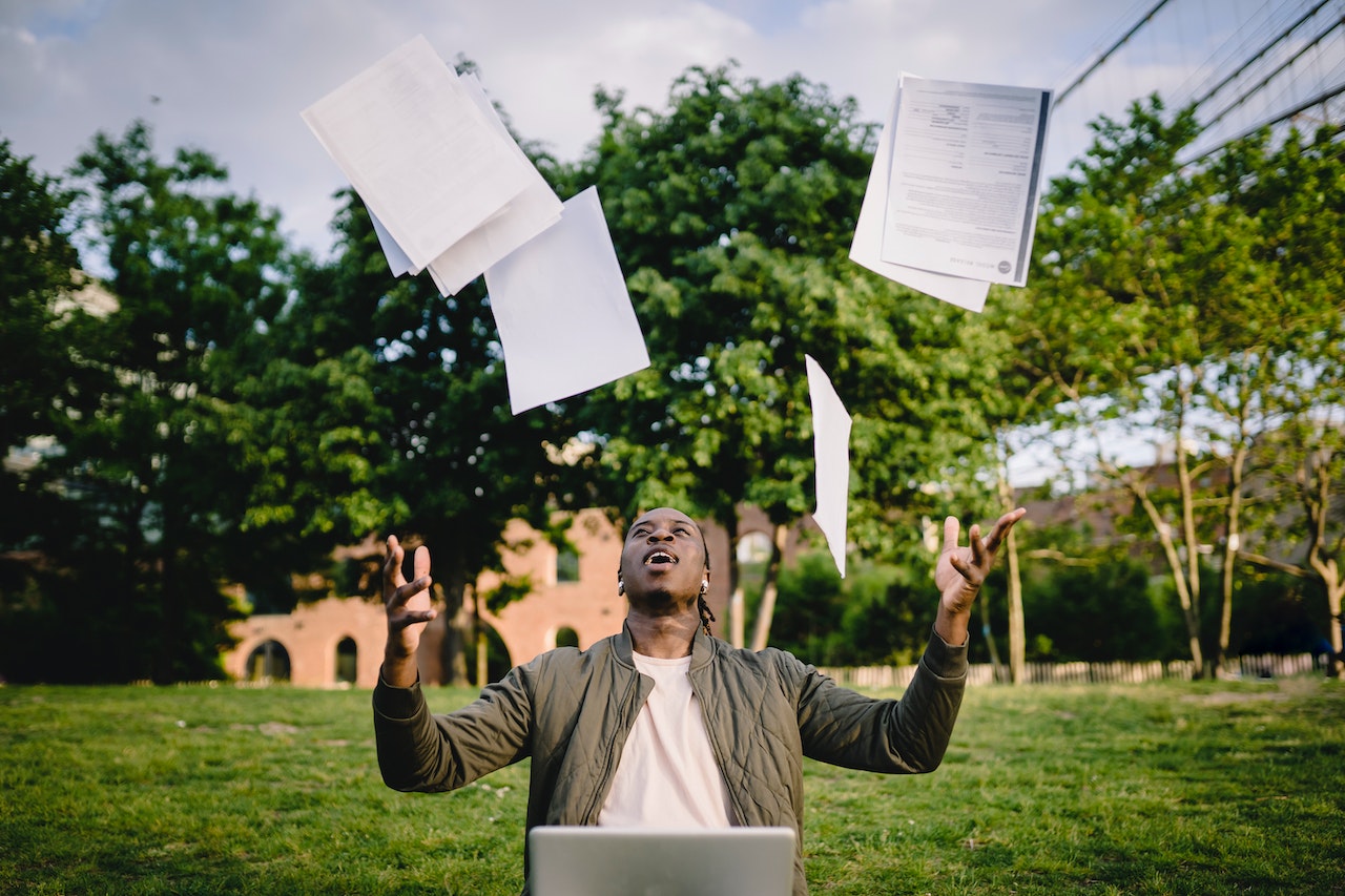 man at laptop throwing paper resumes into air